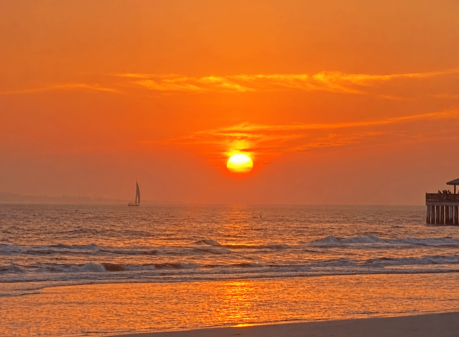 Golden sunset over the ocean, with a sailboat on the horizon